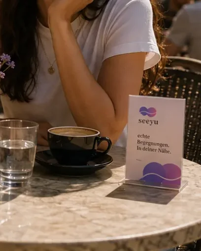 Seeyu-Aufsteller auf einem Cafétisch, daneben Kaffee und ein Glas Wasser
