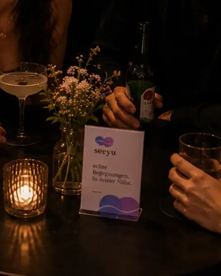 Seeyu-Aufsteller auf einem Partytisch, daneben Kerze, Blumen und Drinks